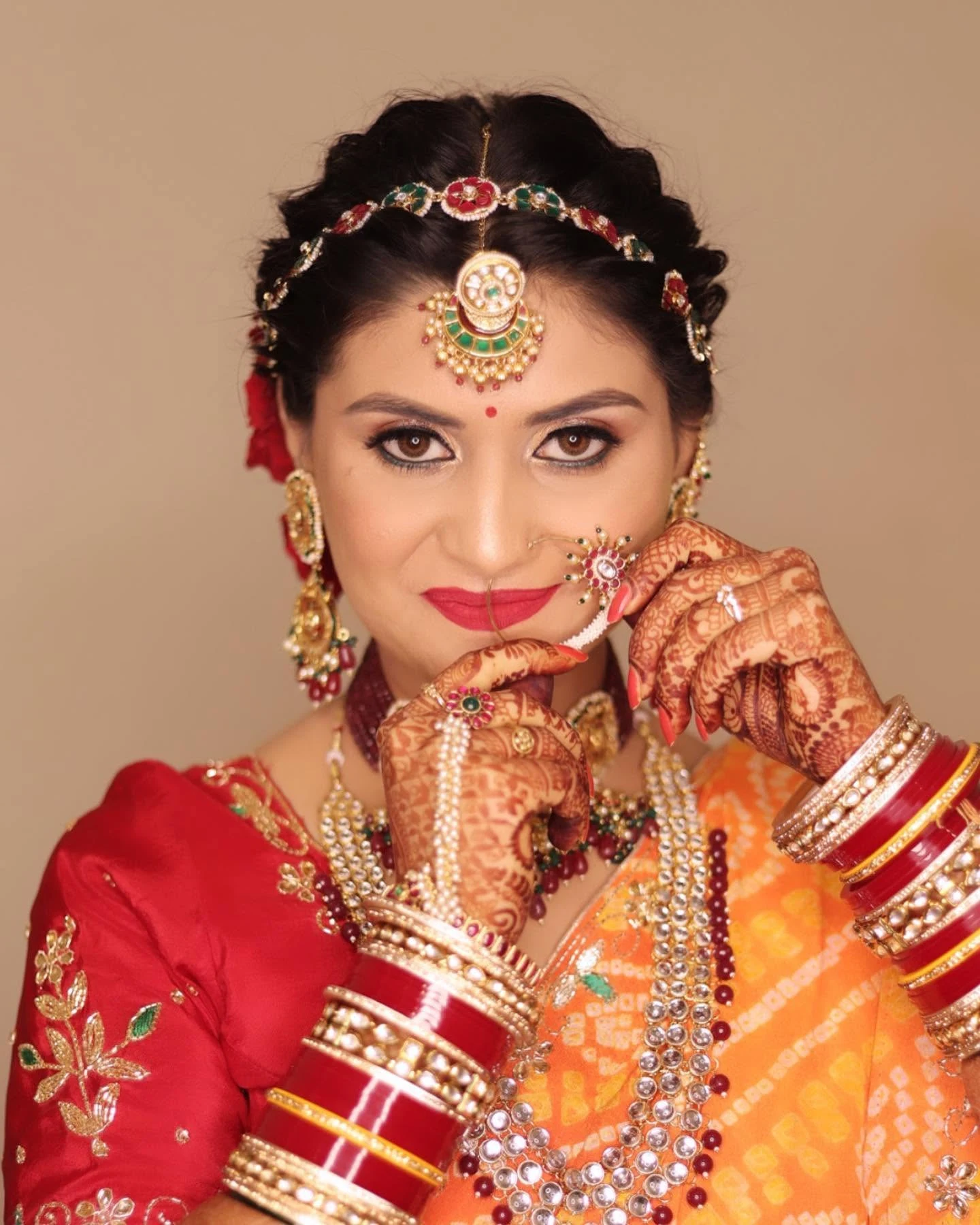Bride in a red and orange saree with traditional jewellery and intricate mehndi.