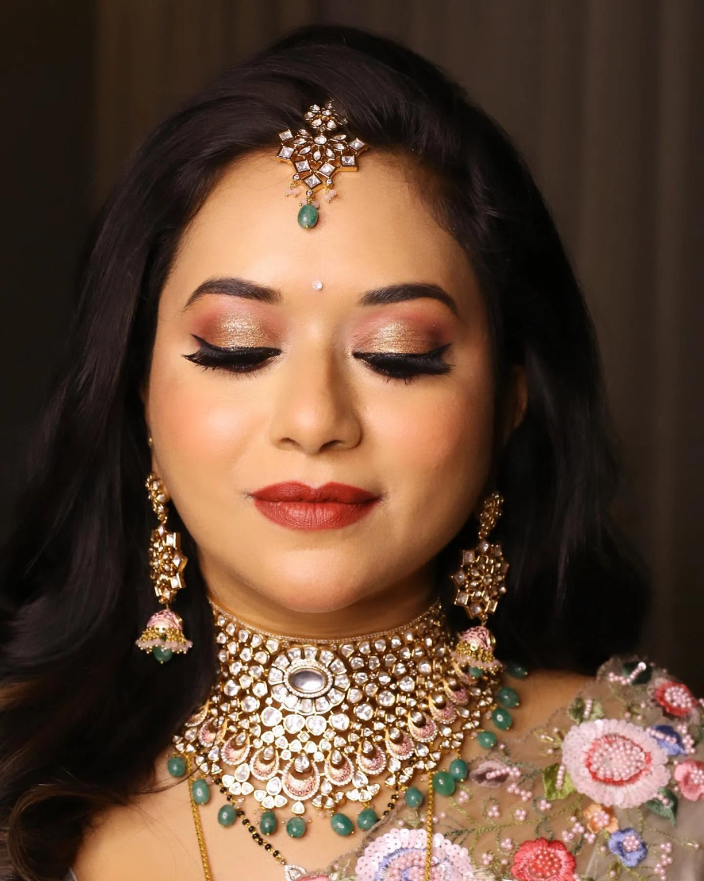 Portrait with closed eyes showing shimmering eyelids, a red lip and kundan jewellery.