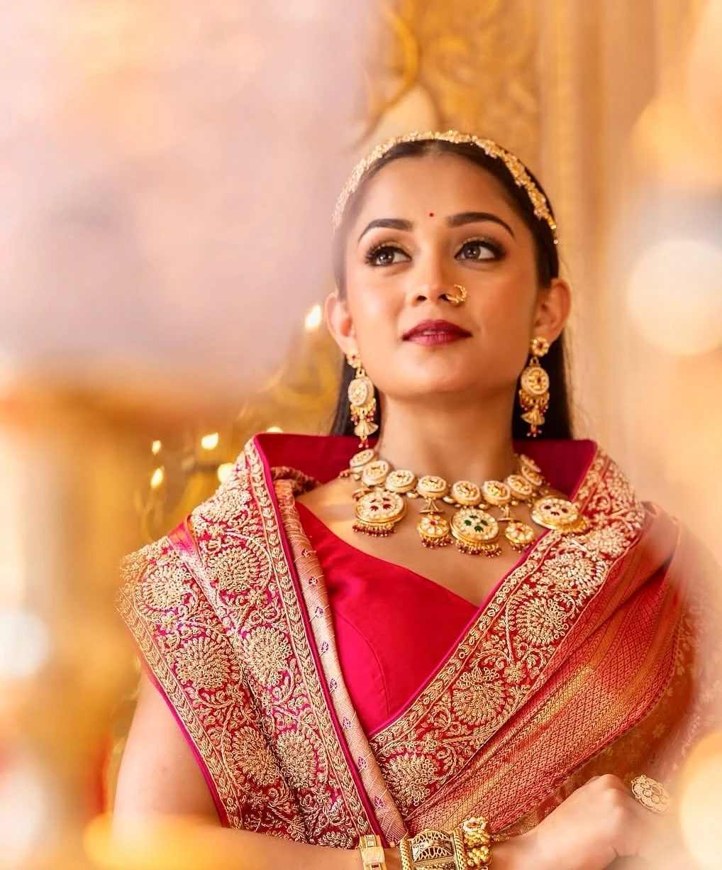 Bridal portrait in a red and gold saree with traditional gold jewellery.