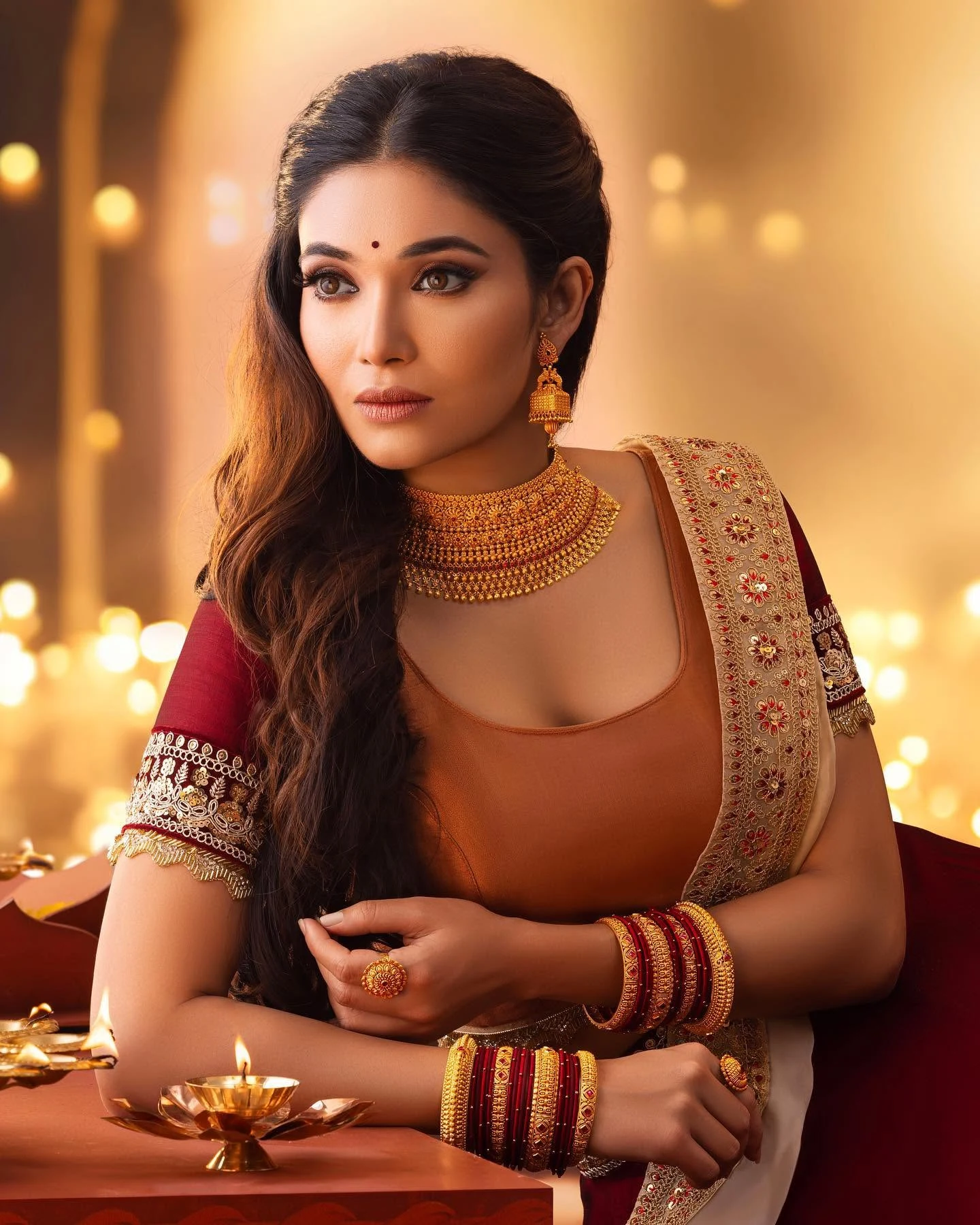 Portrait with softly waved hair, defined eyes and gold jewellery in warm lighting.