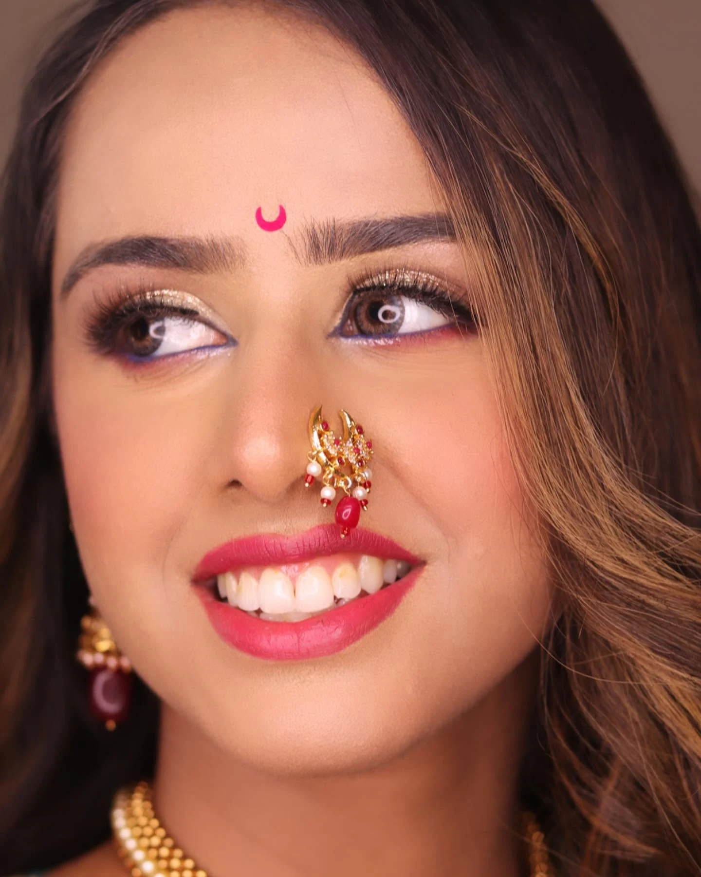 Close-up of a smiling bride with pink lips, defined eyes and a traditional nose ring.