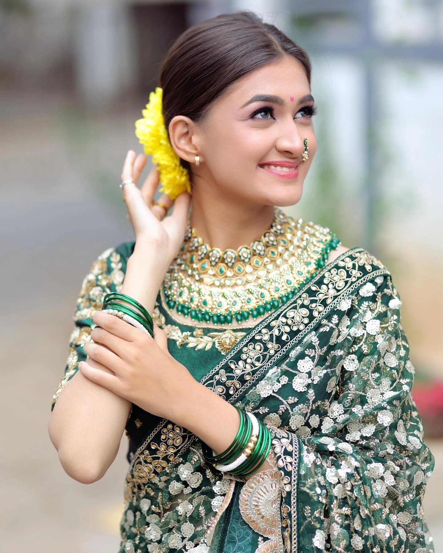 Smiling bride in a green saree with yellow flowers in her hair and green-and-gold jewellery.